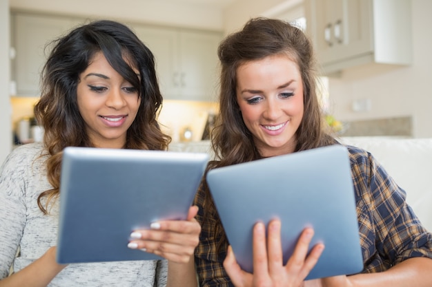 Photo deux femmes souriantes tenant et en regardant les tablettes