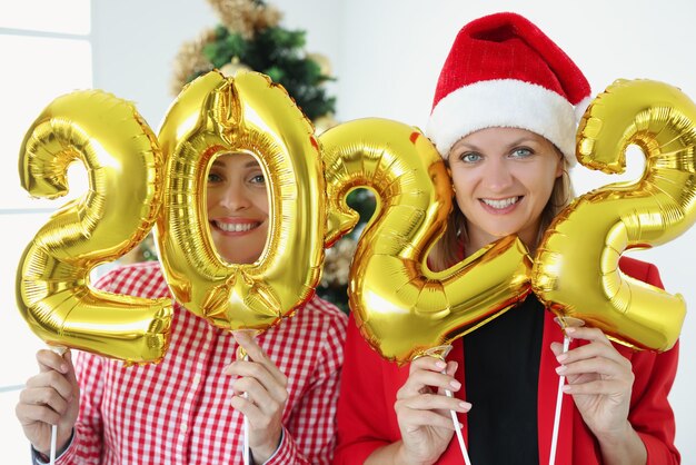 Deux femmes souriantes tiennent des numéros sur fond d'arbre du nouvel an bonne année et noël