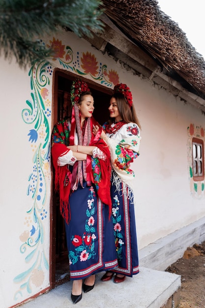 Deux femmes ukrainiennes vêtues de vêtements ethniques traditionnels et d'une couronne rouge florale sur fond de hutte décorée Robe brodée nationale ukrainienne appellent vyshyvanka Priez pour l'Ukraine