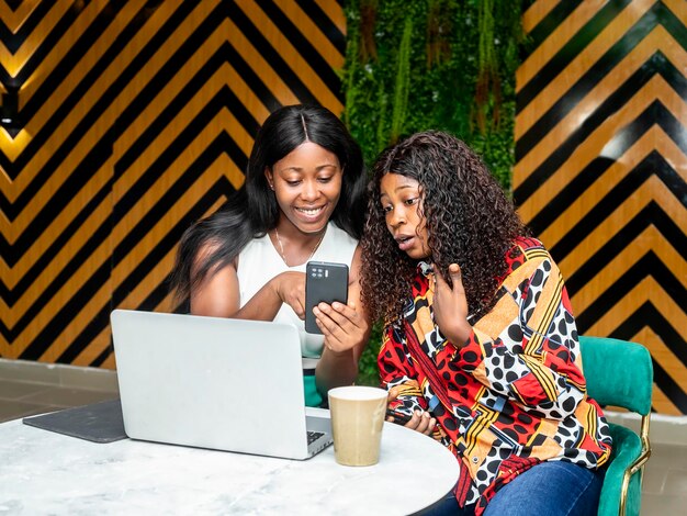 Deux femmes utilisant un ordinateur portable vérifiant leur téléphone portable dans un café