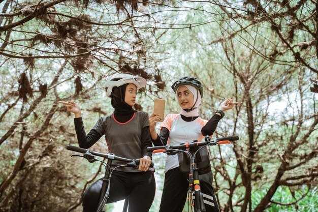 Deux femmes à vélo avec des gestes de la main pointant dans des directions opposées tout en regardant une carte numérique sur un téléphone portable