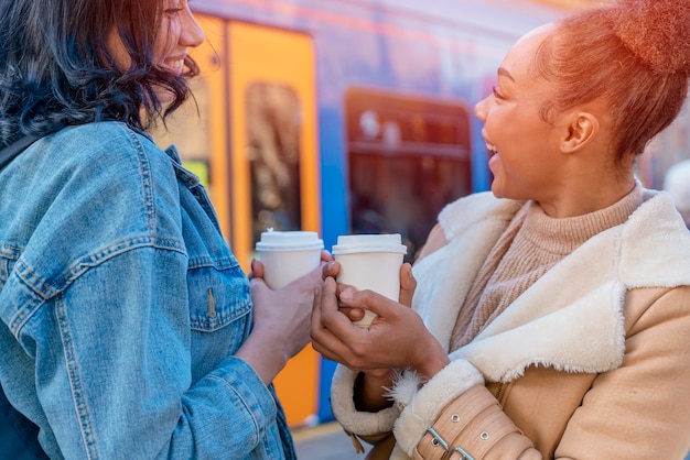 Deux femmes en veste en jean se parlent en buvant du café et en attendant un tram