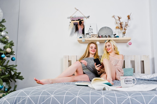 Photo deux fille blonde elegante porter sur une tunique chaude assis sur le lit.