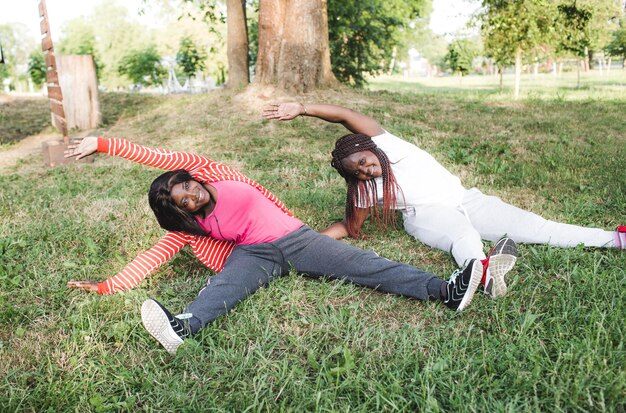 Deux filles afro-américaines font du sport et font des exercices assis dans le parc sur l'herbe.