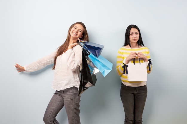 Deux filles après le shopping. L'un d'eux est heureux de tenir beaucoup de sacs et un autre ne tient malheureusement qu'un seul sac.