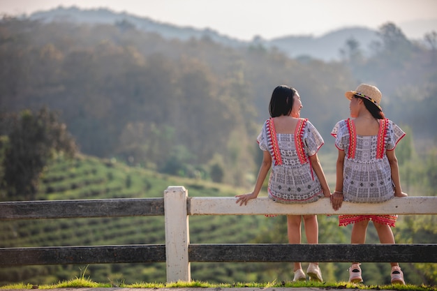 Deux Filles Asiatiques Mignonnes Et Jeunes Assis Sur La Barrière De Jardin Au Coucher Du Soleil