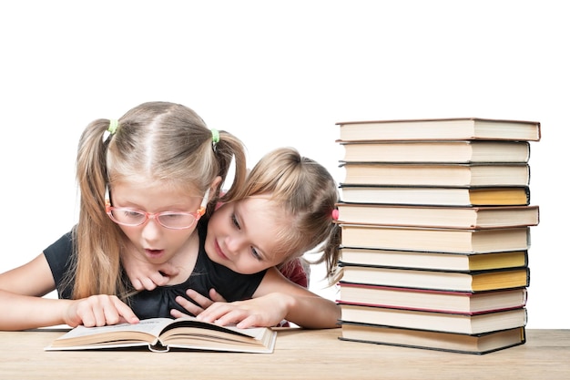 Photo deux filles assises à un bureau avec une pile de livres surpris en train d'étudier un livre ouvert isolé sur fond blanc