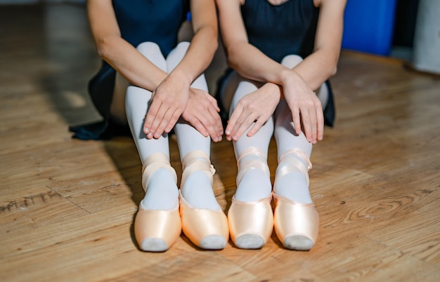 Deux filles de ballet mettent des chaussons de pointe alors qu'elles sont assises sur le plancher en bois. Les danseurs de ballet ont attaché des chaussures de ballet. Fermer