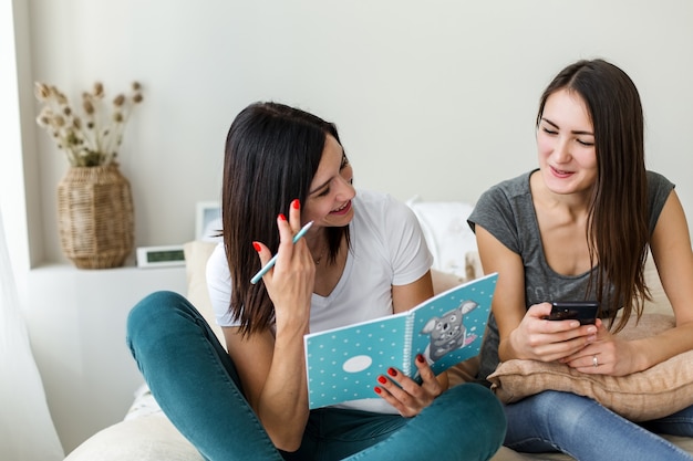 Deux filles brunes sont assises à parler, tenant un livre et un téléphone.