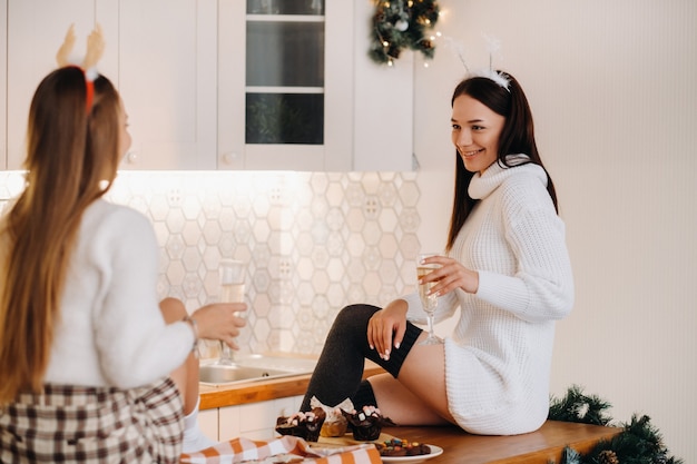 Deux filles dans un environnement familial confortable dans la cuisine avec du champagne à la main pour Noël. Les filles souriantes boivent du champagne lors d'une soirée festive