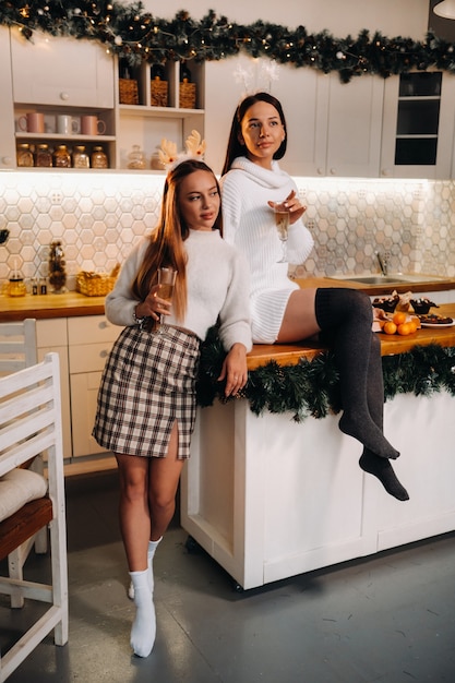 Deux filles dans un environnement familial confortable dans la cuisine avec du champagne à la main pour Noël. Les filles souriantes boivent du champagne lors d'une soirée festive