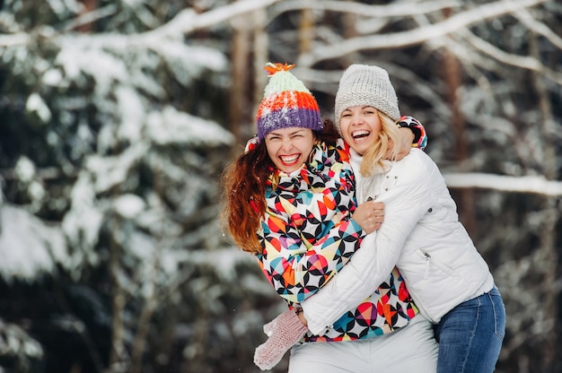 Deux filles dans la forêt d'hiver étreignent et sourient émotionnellement. Des femmes heureuses étreignent et expriment leur joie