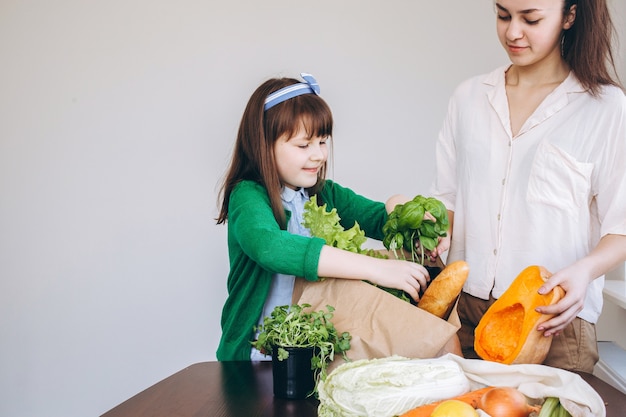 Deux filles déballant un sac écologique avec des légumes, des verts sans plastique sur fond blanc. Zéro déchet, concept écologique sans plastique.