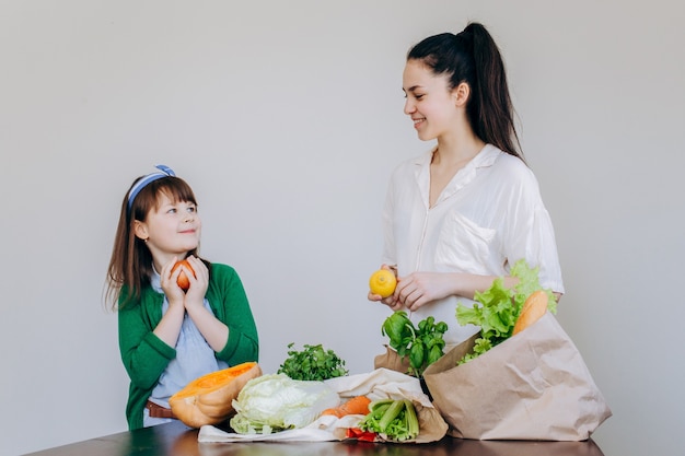 Deux filles déballant un sac écologique avec des légumes, des verts sans plastique sur fond blanc. Zéro déchet, concept écologique sans plastique.