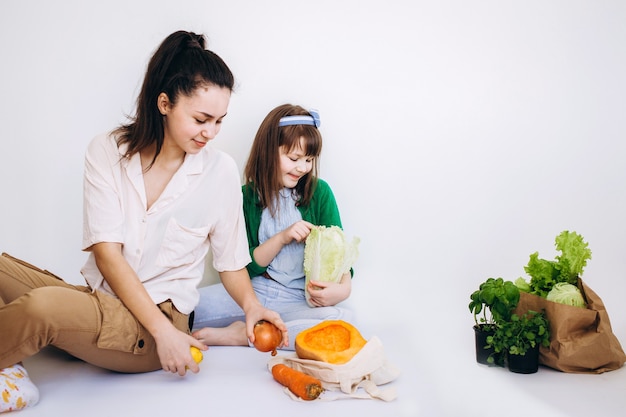 Deux filles déballant un sac écologique avec des légumes, des verts sans plastique sur fond blanc. Zéro déchet, concept écologique sans plastique.