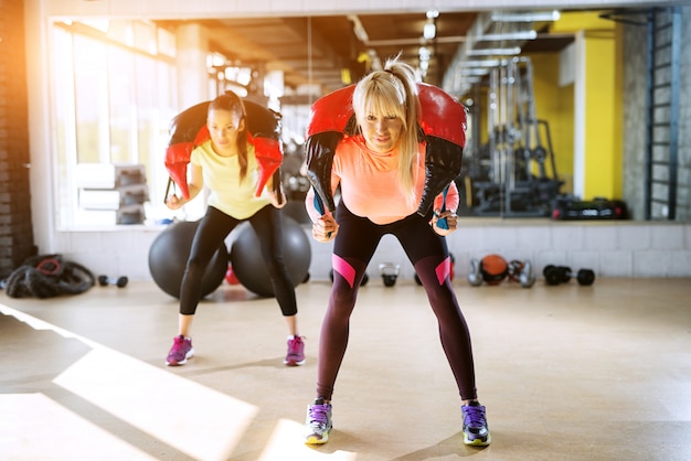 Deux filles en forme concentrées faisant des squats avec un équipement de poids autour du cou.
