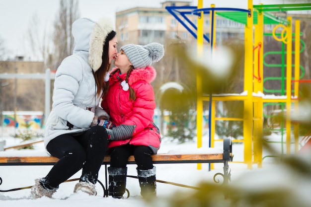 Deux filles heureuse, mère et fille, assis sur un banc dans une aire de jeux dans le parc de la ville.