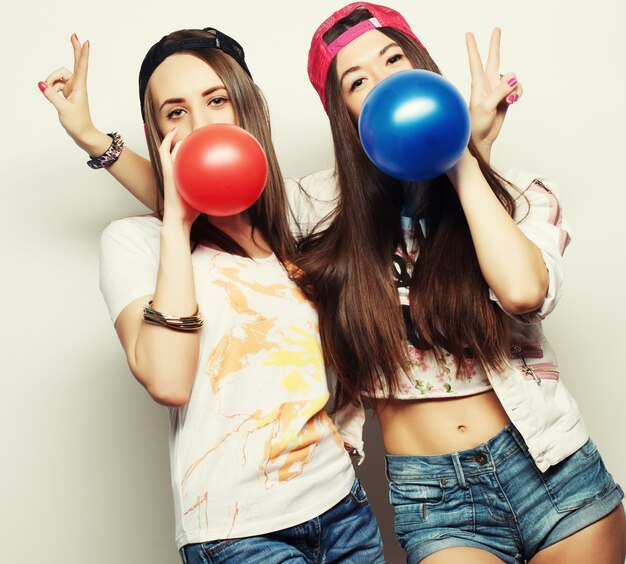 Deux filles heureuses de hipster souriant et tenant des ballons colorés sur fond blanc