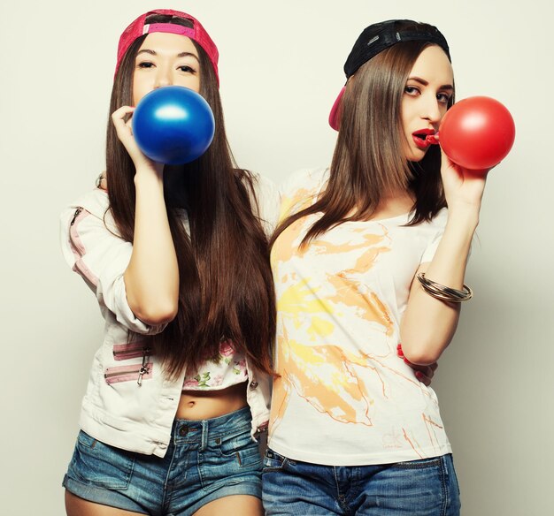 Deux filles hipster heureuses souriant et tenant des ballons colorés sur fond blanc