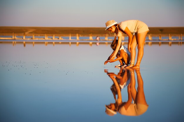 Deux filles incroyablement belles dans des tenues inhabituelles sur un magnifique lac salé transparent recherchent quelque chose dans une surface brillante