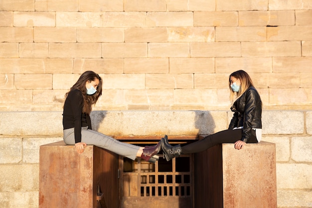 Deux filles avec un masque facial maintenant la distance sociale en étendant leurs jambes. Ils sont à l'extérieur.