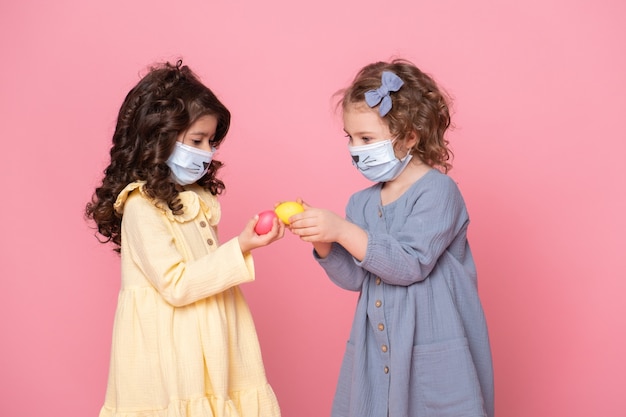 Deux filles en masque de protection avec des oeufs colorés sur rose