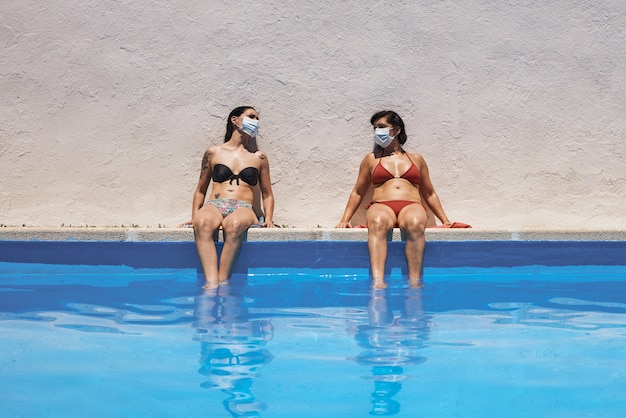 Deux filles avec des masques assis dans la piscine en train de bronzer