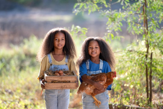 Deux filles noires tiennent un poulet brun dans leur étreinte d'amour avec les yeux fermés Une petite fille noire tient une poule dans une ferme