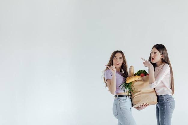 deux filles pensant quoi acheter sur un fond blanc avec un panier et un paquet de nourriture