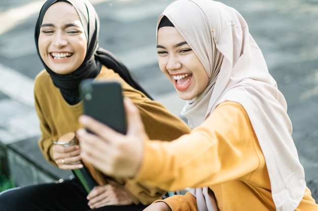 Deux filles portant le hijab riant en regardant une vidéo avec un smartphone l'après-midi dans le parc