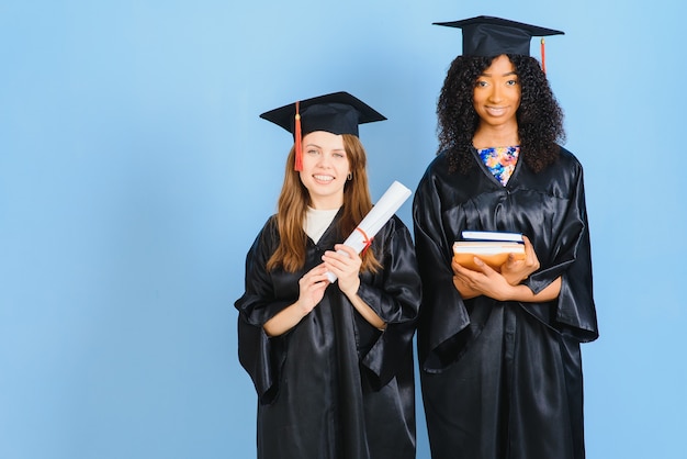 Deux filles posent pour prendre une photo en robe noire et détiennent un diplôme.