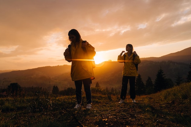 Deux filles randonneurs en vestes jaunes escaladent la montagne sous la pluie sur fond de beau coucher de soleil
