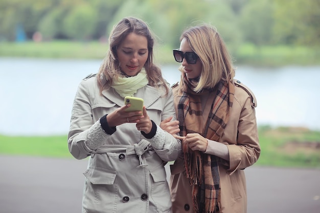 deux filles regardent le téléphone promenade d'automne / manteau de parc de la ville d'automne, mode d'automne, style, look, vêtements