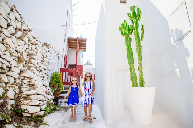 Deux filles en robes bleues s'amuser en plein air. Enfants à la rue du village traditionnel grec typique avec des murs blancs et des portes colorées sur l'île de Mykonos, en Grèce