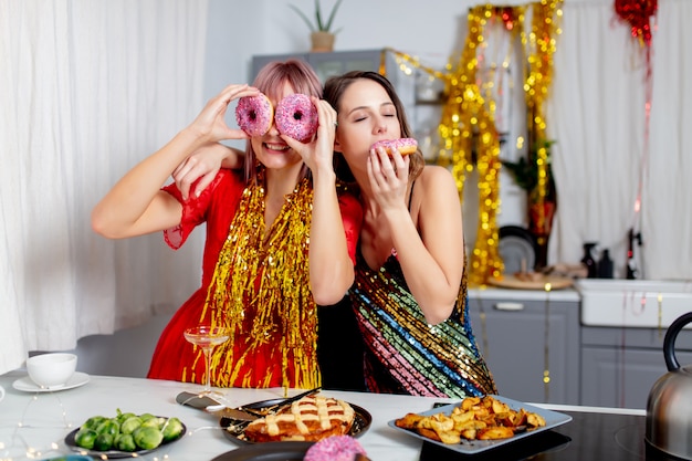 Deux filles s'amusant avec des beignets dans la cuisine après une fête