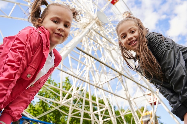 Photo deux filles s'amusent dans un parc d'attractions. une roue ferris est en arrière-plan.