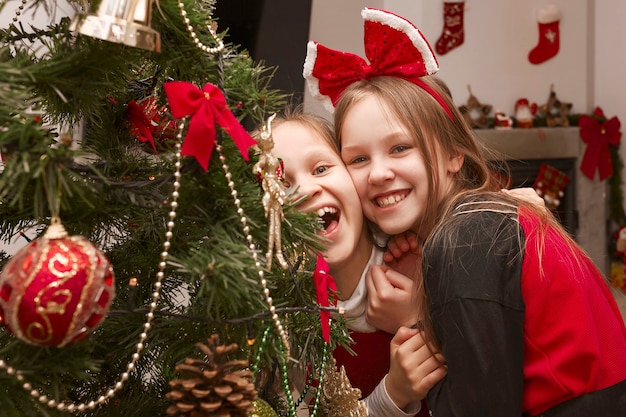 Deux filles se réjouissent et rient dans une robe de Noël près d'un arbre de Noël décoré