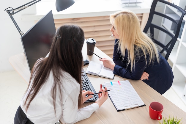 Deux filles se tiennent dans le bureau près de la table et regardent l'écran.