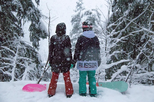Photo deux filles avec un snowboard dans la forêt dans les montagnes et les chutes de neige