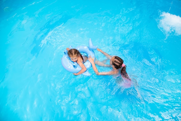 Deux filles sœurs de 11-13 et 6 ans nagent dans une piscine à l'eau bleue et ont un ventilateur. La fille aînée a des tresses africaines tressées avec des rubans zi-zi. Été. Vacances en famille.