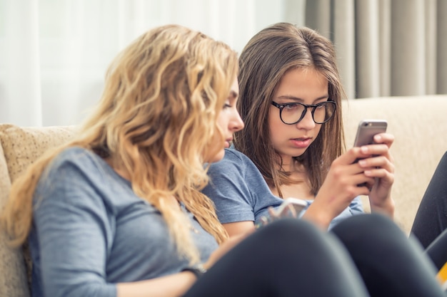 Deux filles ou sœurs adolescentes utilisant des téléphones intelligents dans le salon.