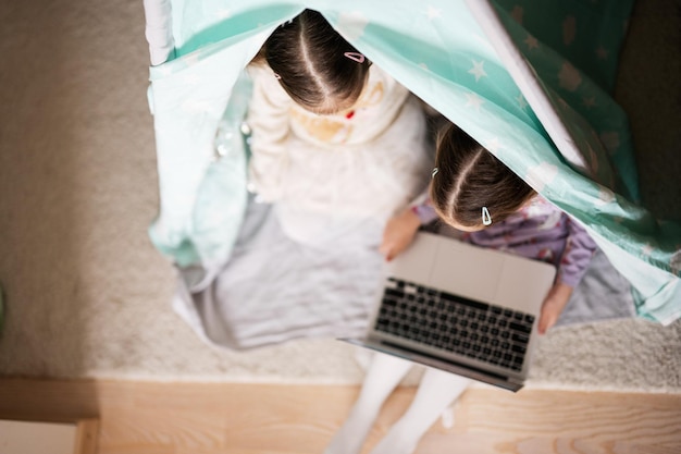 Deux filles sœurs regardant sur un ordinateur portable à la tente du wigwam Technologie et concept de maison