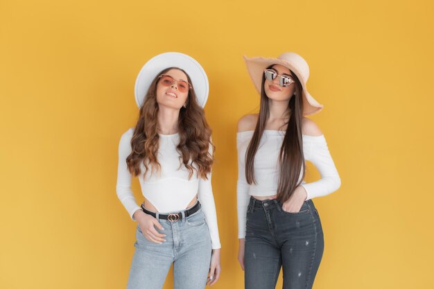 Deux filles souriantes à lunettes de soleil posant ensemble et regardant la caméra sur jaune