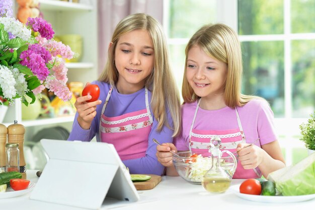 Deux filles en tabliers roses préparant une salade sur une table de cuisine avec tablette