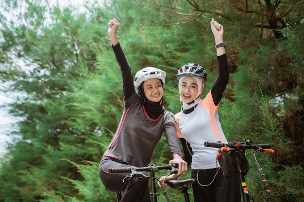 Deux filles voilées souriant avec les poings serrés tout en faisant du vélo ensemble