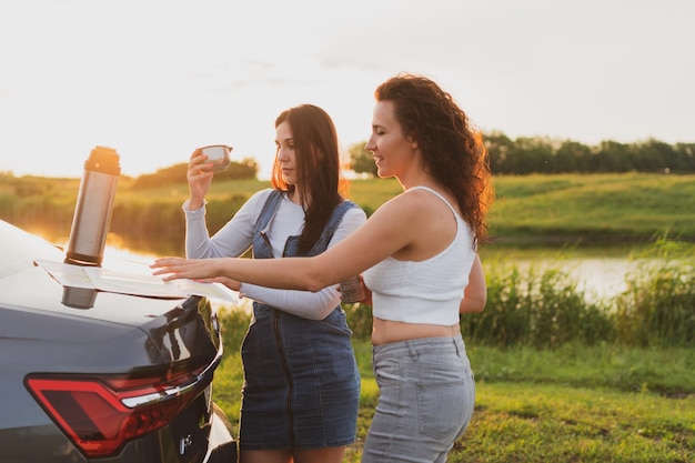 Deux filles voyagent sur les routes en voiture arrêtée au bord de la route et regardent la carte en buvant du café à partir d'un concept de vacances thermos