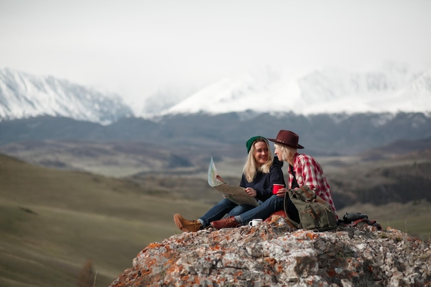 Deux filles voyageuses avec une carte assises sur un rocher dans les montagnes