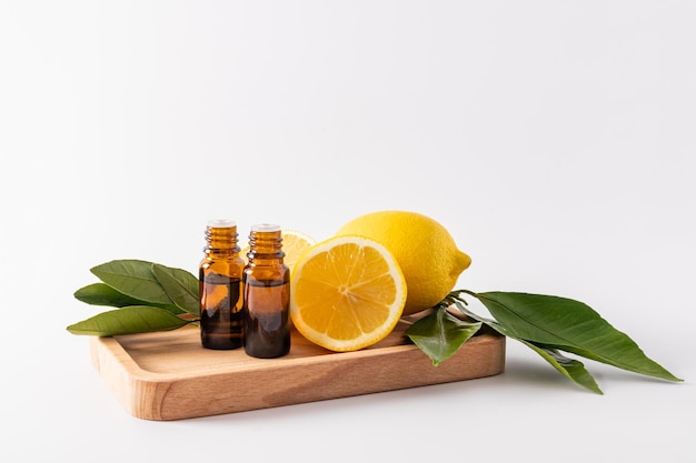 Deux flacons médicaux avec un compte-gouttes contenant de l'huile essentielle de citron se tiennent sur un plateau en bois parmi les citrons mûrs aromathérapie massage antioxydant vitamine C