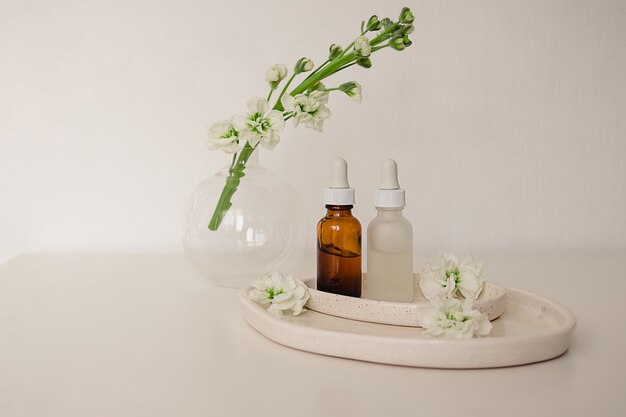 Deux flacons en verre pour cosmétique, médecine naturelle, huile essentielle dans les assiettes en céramique décorées de fleurs et un vase rond sur fond blanc. Concept de produit de beauté écologique.