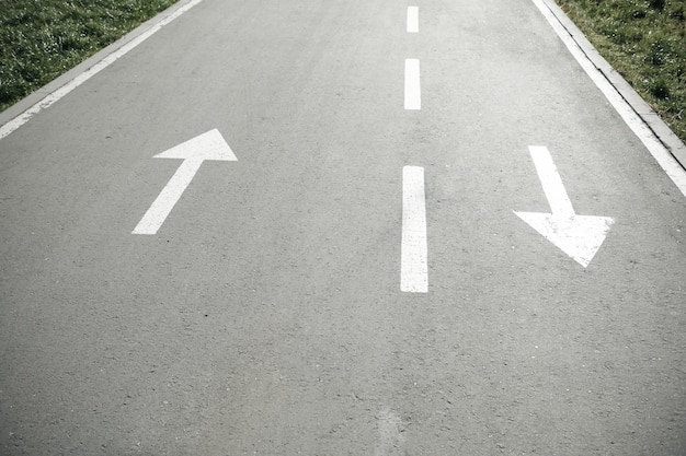 Photo deux flèches blanches dans la direction opposée sur la route goudronnée les deux côtés signent flèches vers le haut et vers le bas direction pour la sécurité routière pointeur sur le sol en asphalte gris